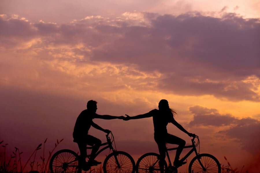 Silhouettes of two cyclists holding hands at sunset, highlighting connection and the beauty of companionship