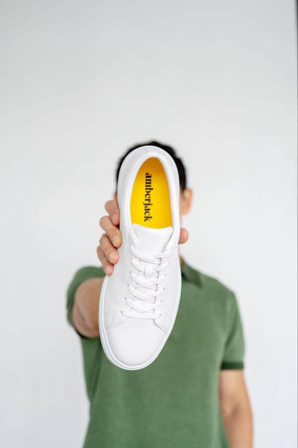 Person in a green shirt holds up an Amberjack Low Top leather sneaker with a yellow insole, highlighting its everyday comfort