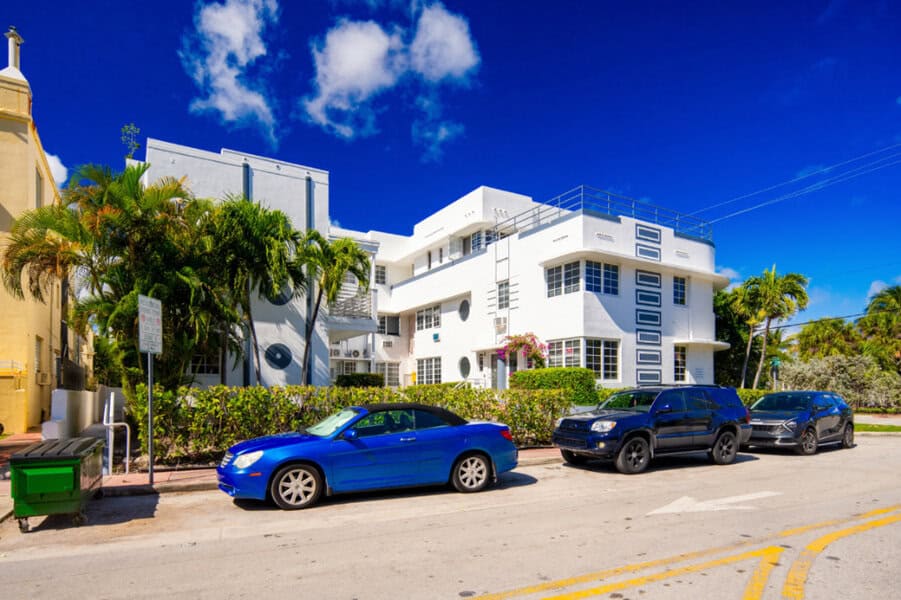 Three cars ideal for luxury car rental in Miami parked on a sunny street lined with palm trees and Art Deco buildings