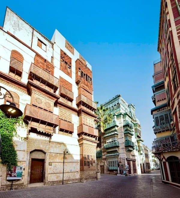 Quiet street in Al-Balad features historic buildings with wooden lattice windows and balconies, ideal for your Jeddah trip under blue skies