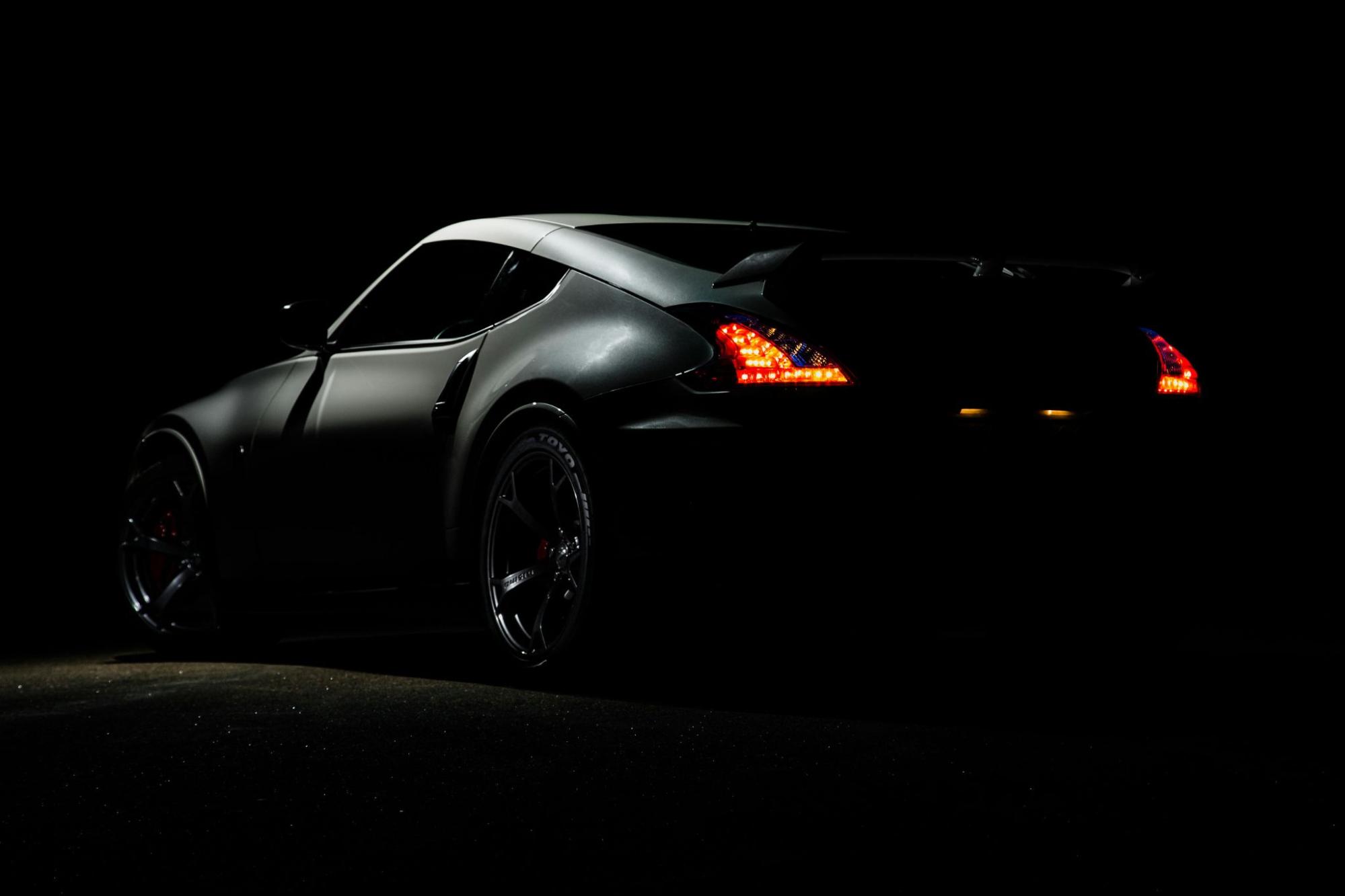 A black luxury sports car with glowing tail lights is partly visible in a dark setting