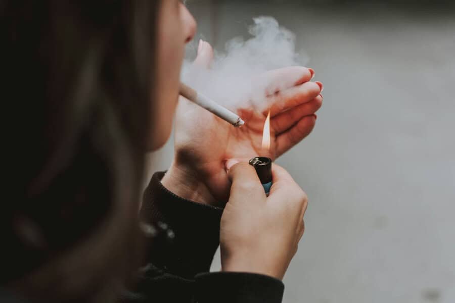 Person lighting a cigarette, hand shielding the flame; smoke rising—habits like this may affect skin health