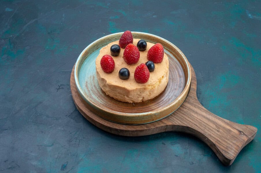 Small round cheesecake topped with berries, ideal for celebrating, served on a ceramic plate with wooden handle