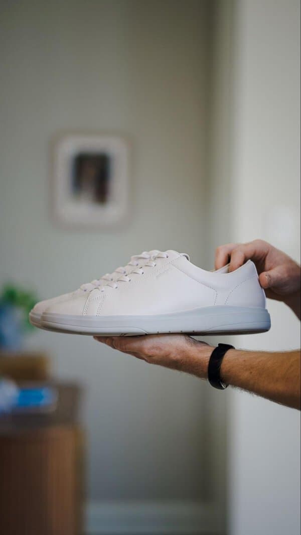 A person holds an Amberjack Low Top leather sneaker in one hand with a blurred indoor background suggesting everyday comfort