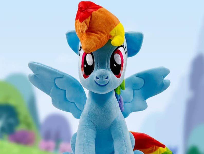 A Rainbow Dash Jumbo plush, blue with wings and rainbow mane, sits outdoors as a cute room décor piece