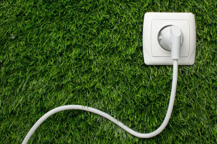 A white electrical plug connects to a wall outlet atop green grass, emphasizing electrical safety with the power cord curving across