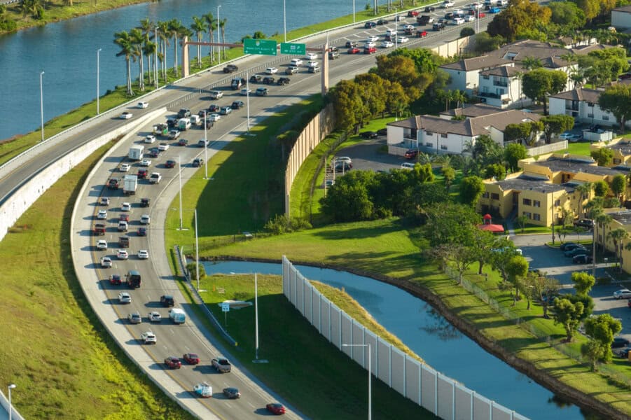 Aerial shot of a lively highway, cars, water canal, green grass, and luxury car rental Miami vehicles close to residential houses
