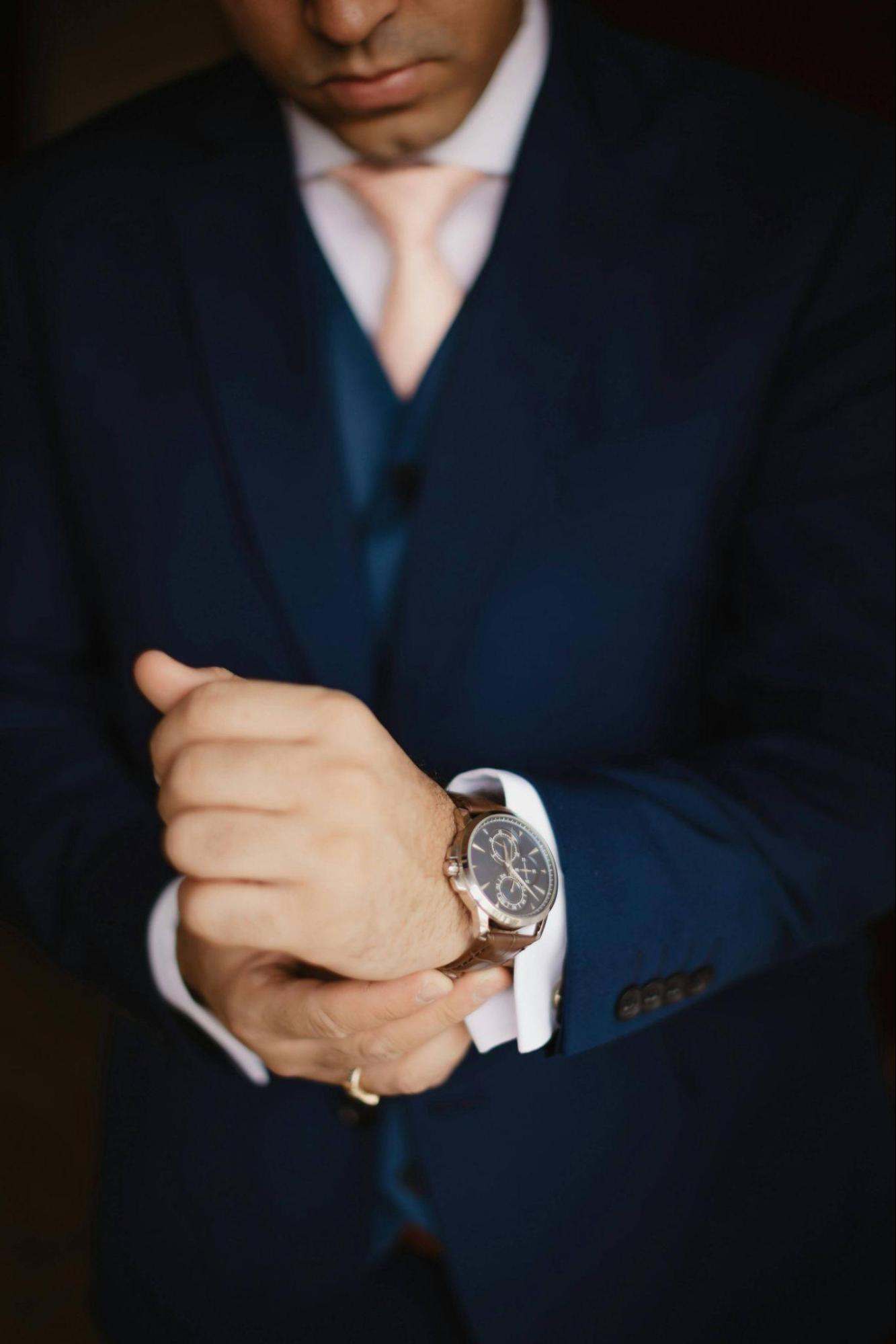A man in a navy suit adjusts his watch mid-frame, capturing the time-efficient elegance of luxury travel