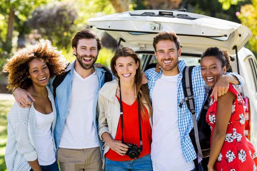 Five friends smiling beside an open car trunk, ideal to test photo editing techniques for fixing incomplete group photos