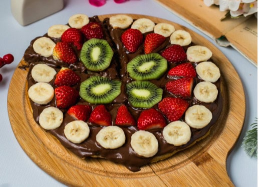 Pizza topped with chocolate spread, banana, strawberries, and kiwi—one of our most crowd-pleasing treats on a wooden board