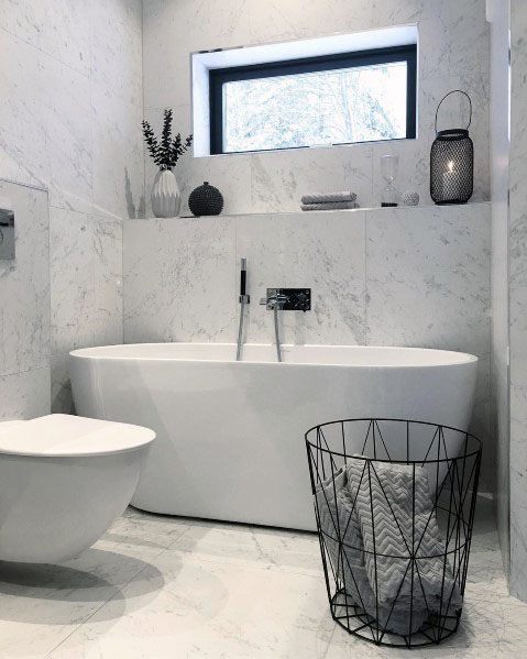 Modern bathroom with marble walls, freestanding tub, and black wire basket decor.