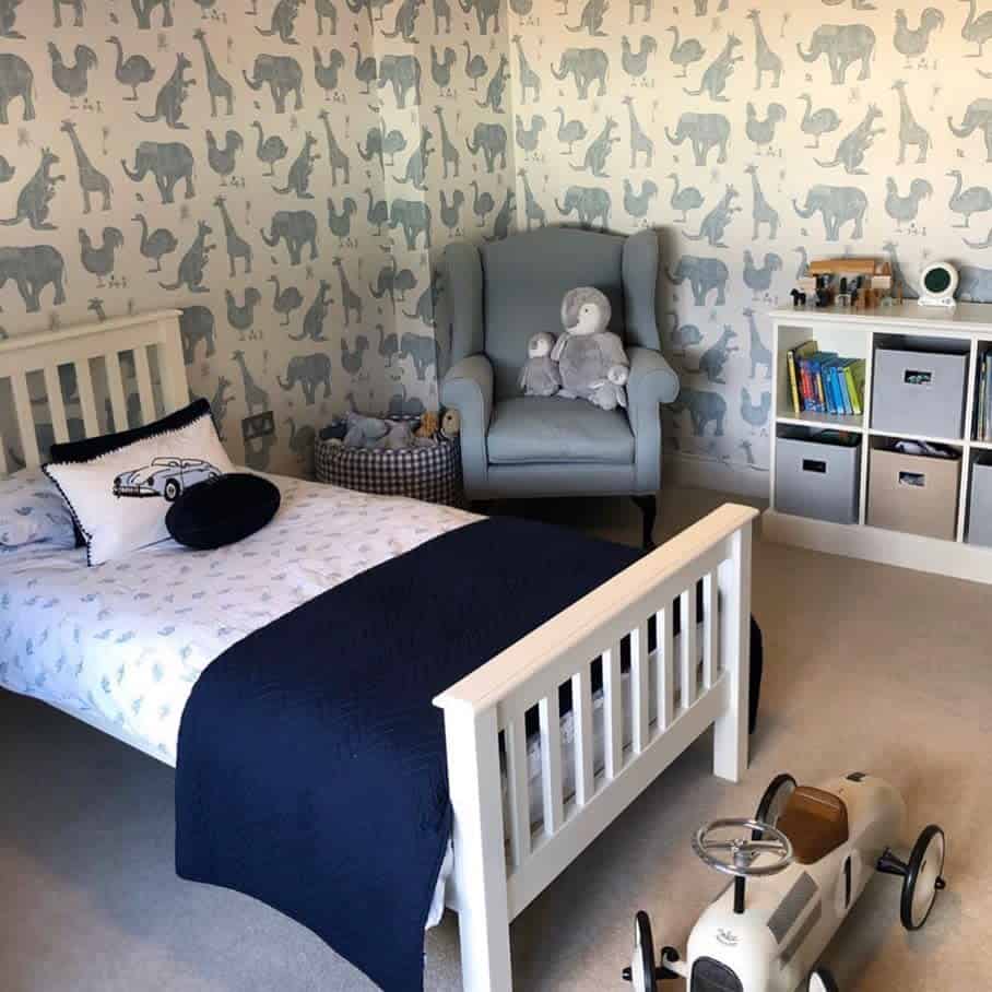 Boys' bedroom with animal wallpaper, white bed, gray armchair, and vintage toy car.