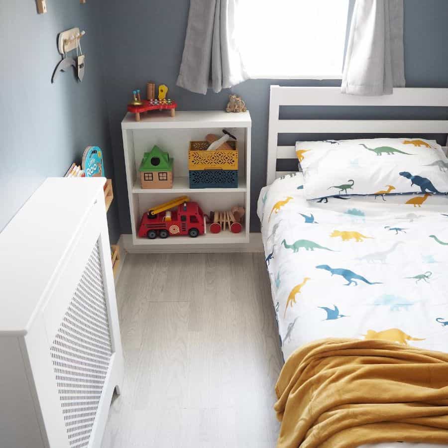 Kids' room with dinosaur bedding, bedside storage shelves, and toys.