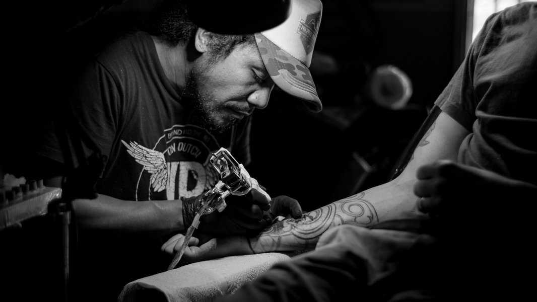 Tattoo artist in a cap working on a forearm tattoo - 5 Tips on How to Edit My Paper Tattoo: Pre-Ink Polishing Tips for Perfecting Your Design Before the Artist's Chair