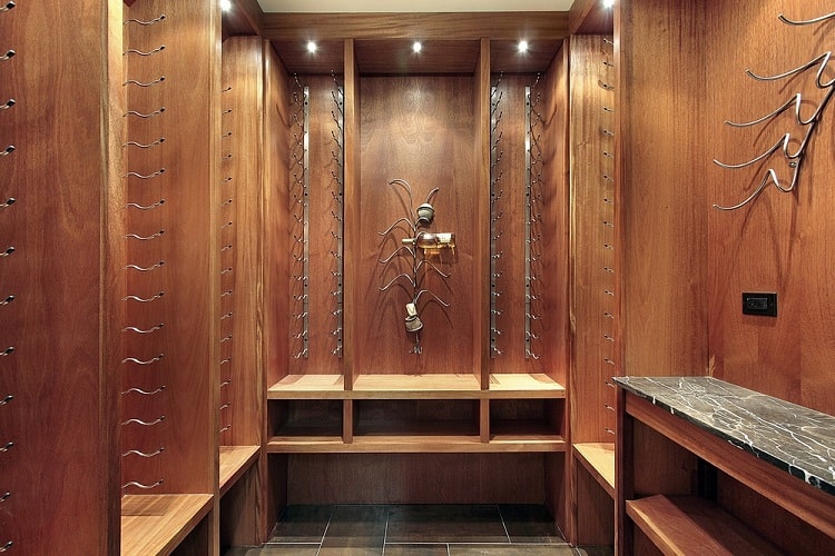 Elegant wine cellar with wooden walls, metal racks, and built-in seating, illuminated by recessed lighting.