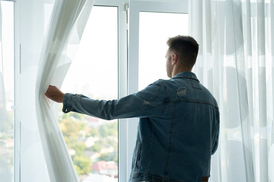 man in a denim jacket is standing at the window