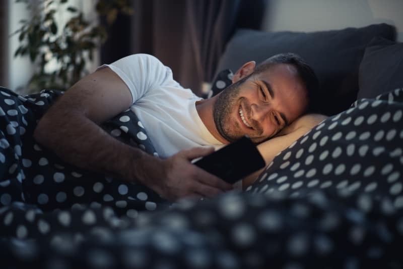 man on the bed smiling while looking at the phone