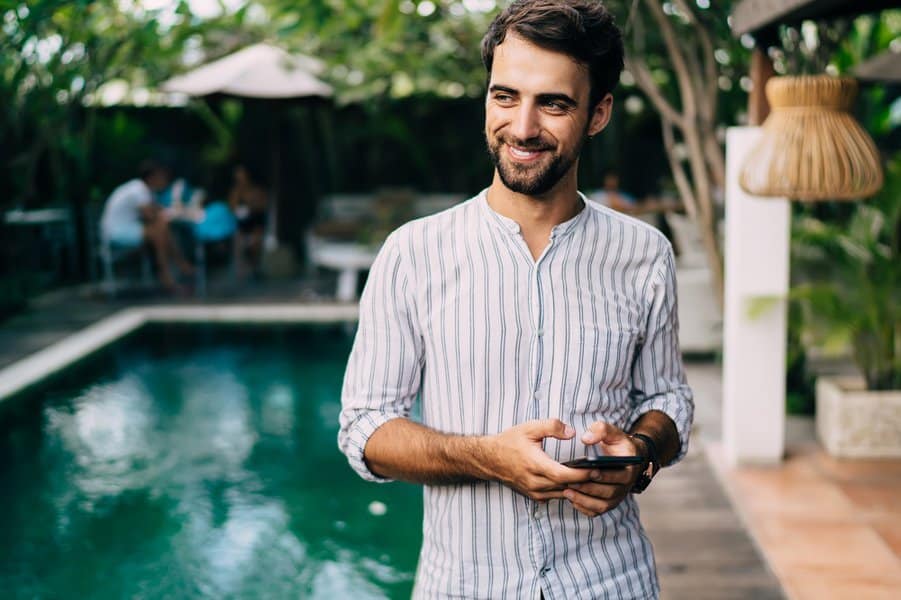 man standing near swimming pool while using mobile phone