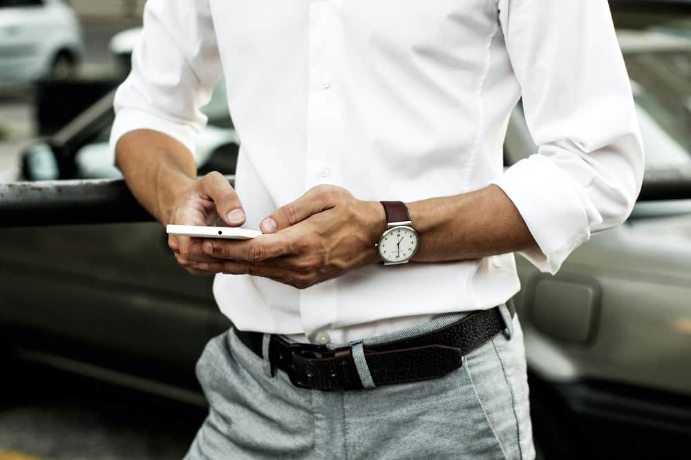 shot of a man using his phone, focused on his black leather belt