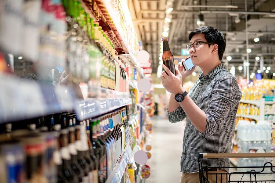  man using smartphone while shopping beer in supermarket