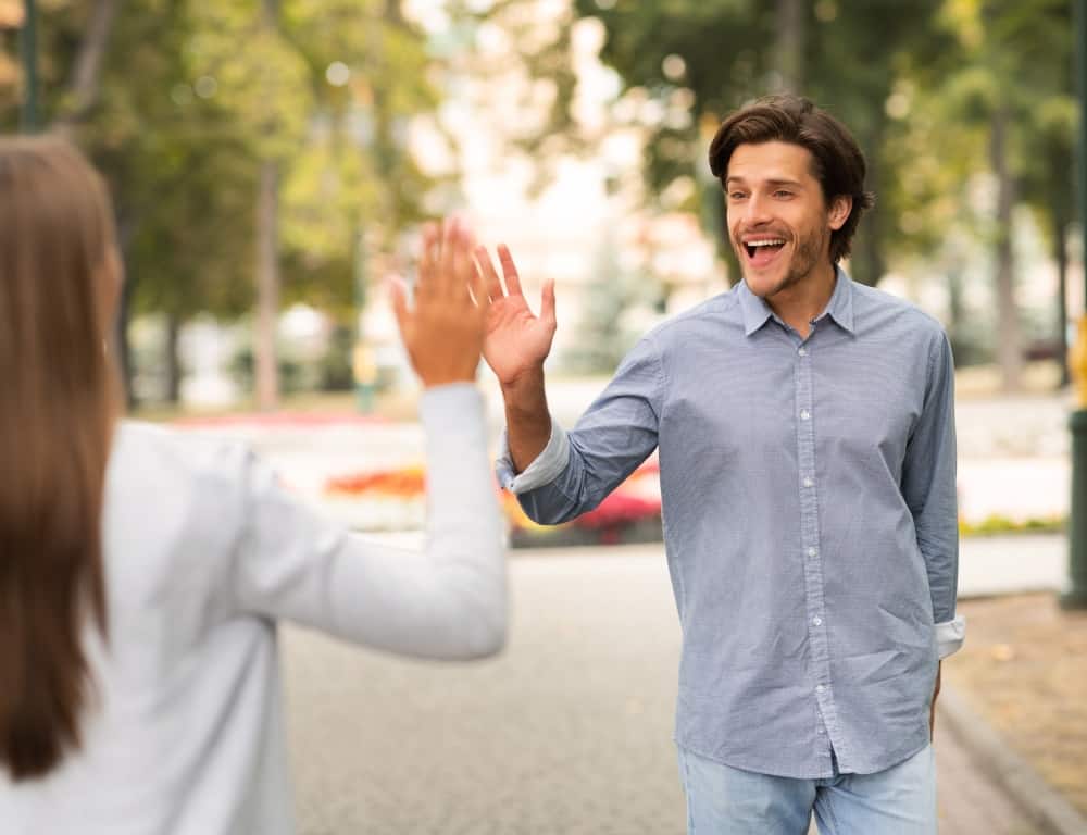 man waving hello meeting his female friend in the park