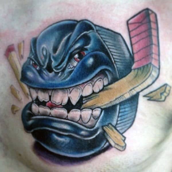 Man With Angry Hockey Puck Chewing Stick Tattoo On Chest