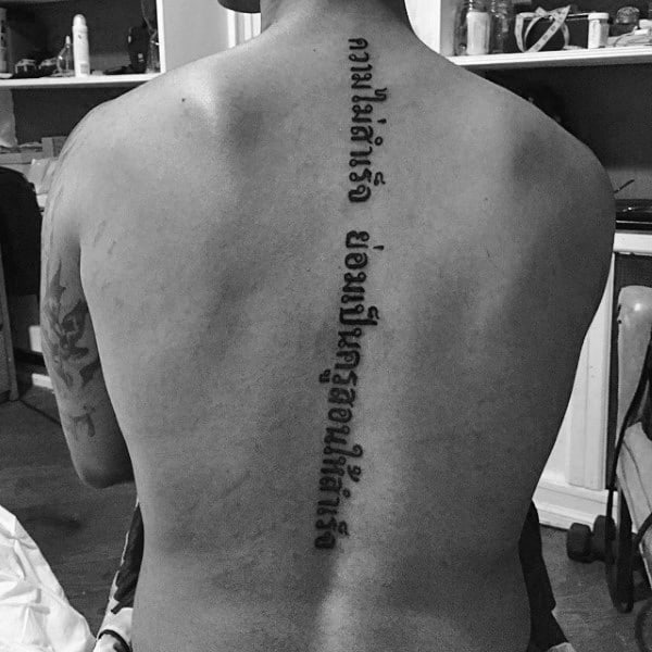 Man With Lettering Center Of Spine Tattoo On Back