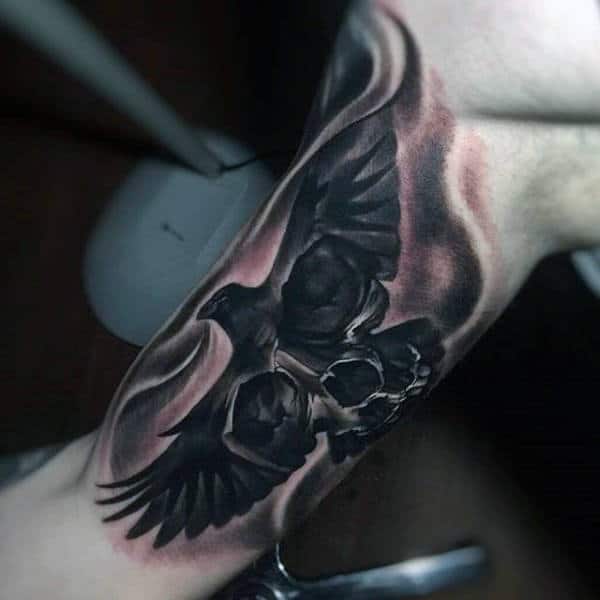 Man With Tattoo Of Crow With Skull On Inner Arm