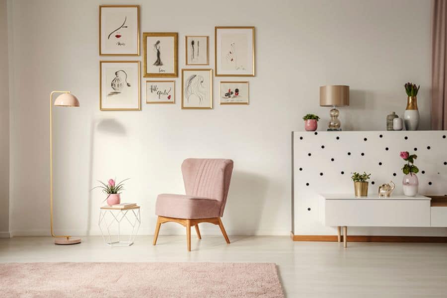 minimalistic living space with pink chair and gold framed wall drawings 