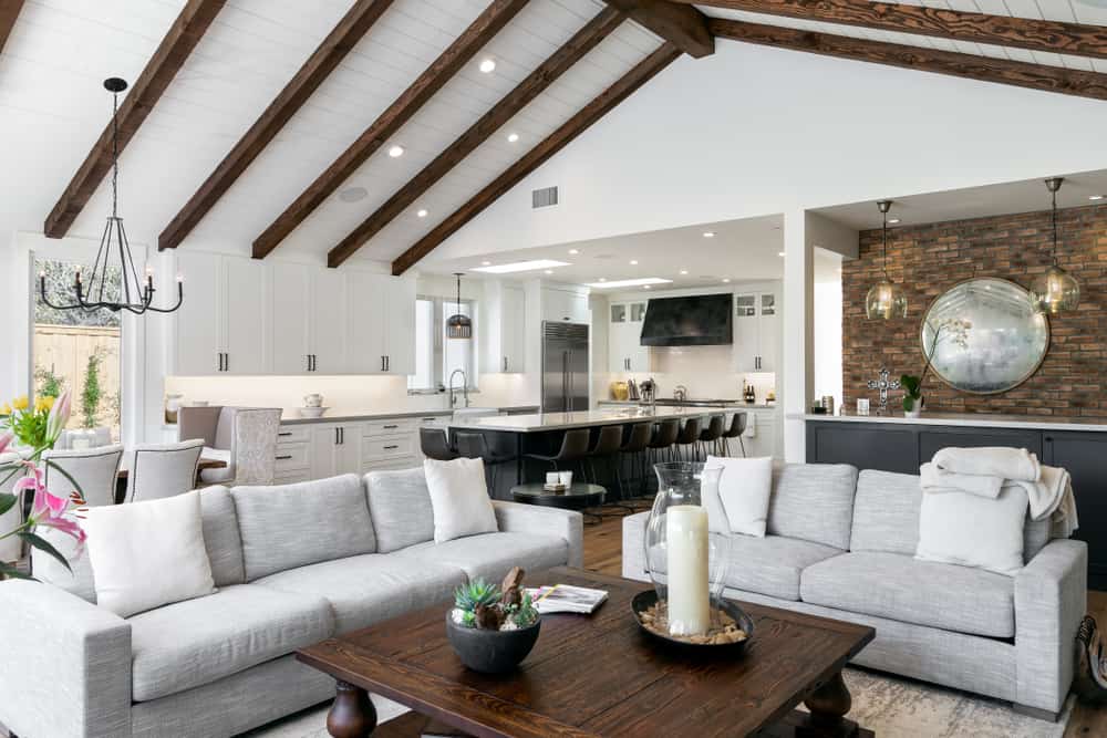 modern farmhouse high ceiling exposed wood beams gray sofas white cabinet kitchen brick wall