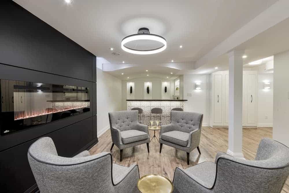 modern basement living room with gray armchairs and electric fireplace 