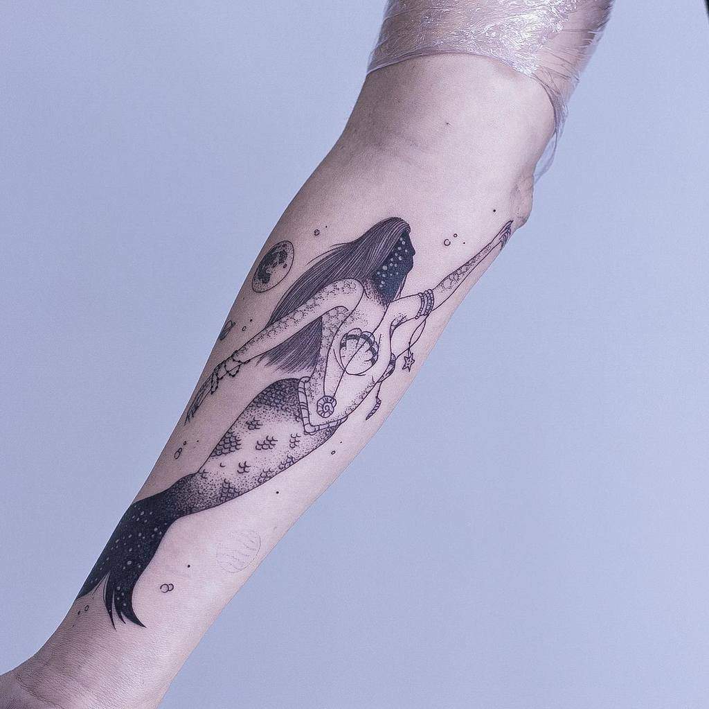 Elegant blackwork tattoo of a celestial mermaid with intricate dot shading, adorned with cosmic details and mystical jewelry