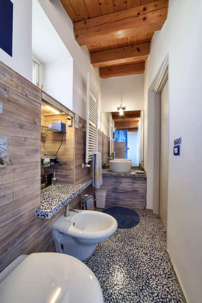 narrow bathroom with wood panel accents and recessed shelving 