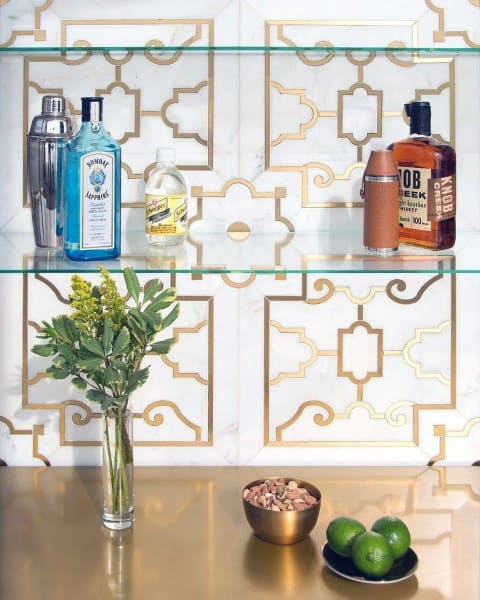 Elegant mini bar with glass shelves, gold-patterned backsplash, and a luxurious golden countertop featuring a vase and small bowls.