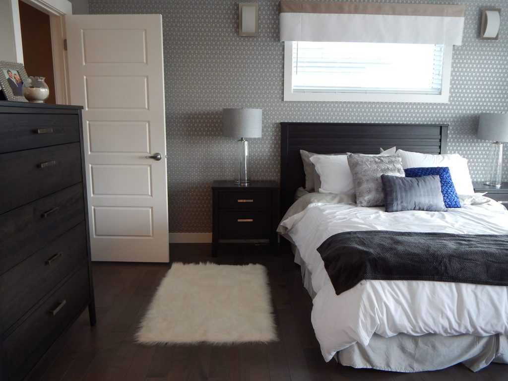 Bedroom with printed wallpaper, black wooden furniture, and dark wood flooring.