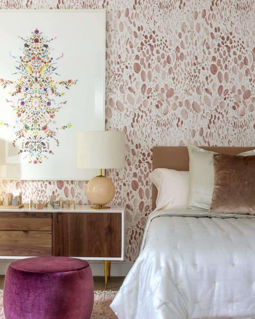 Bedroom with abstract wallpaper, colorful wall art, vintage cabinet, and velvet ottoman.