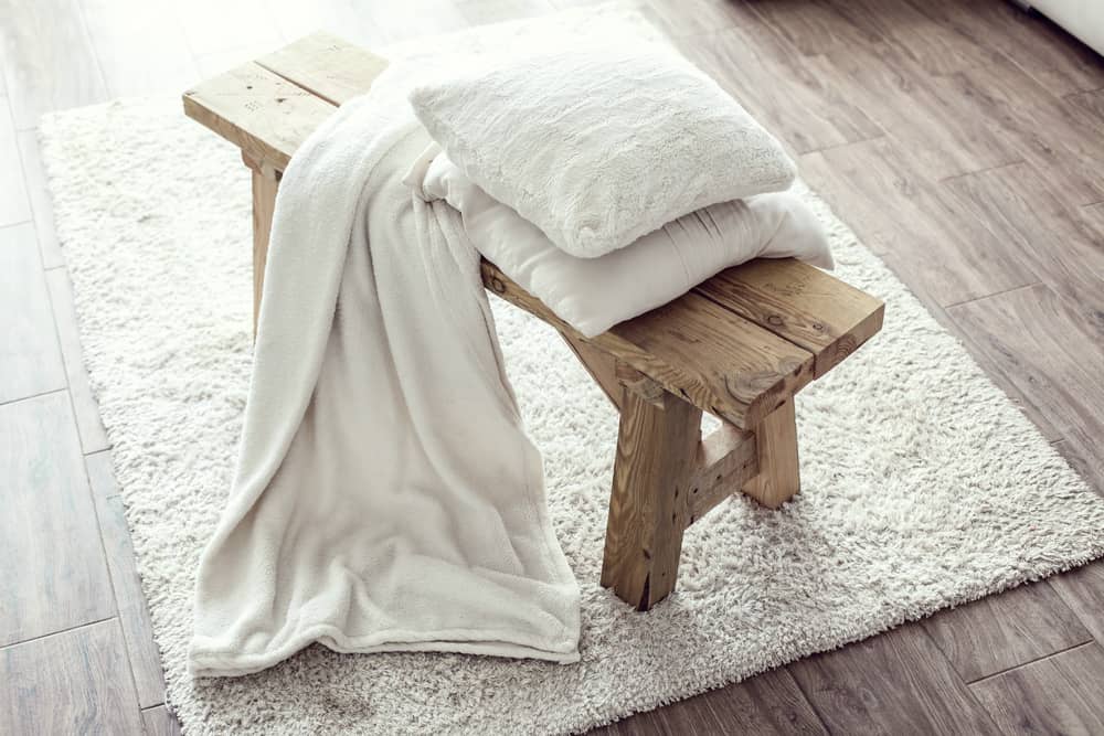 small wood stool with white pillows on white rug