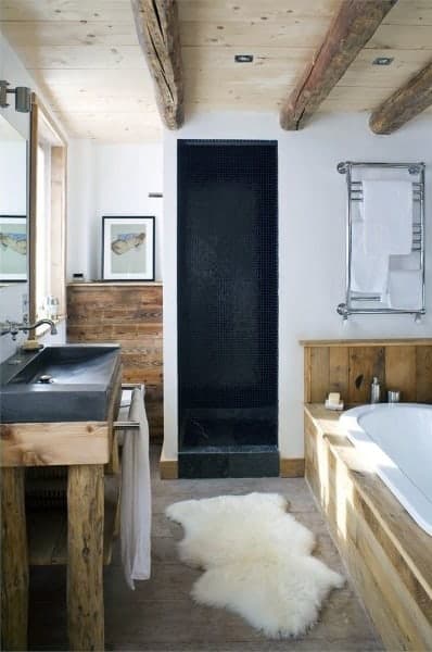 Rustic bathroom with wooden beams, stone sink, black tiled shower, and freestanding tub.