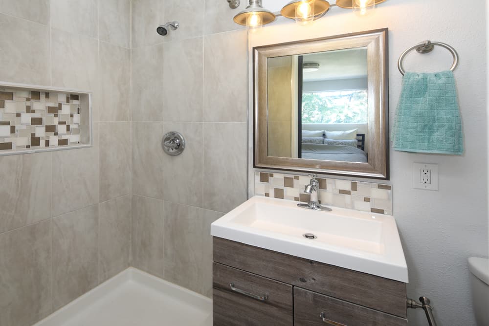 guest bathroom gray shower wall tiles wood vanity white sink 