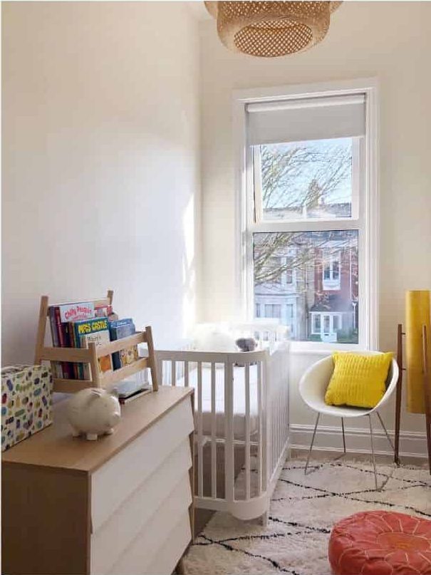 small nursery white crib white chair with yellow pillow window view 