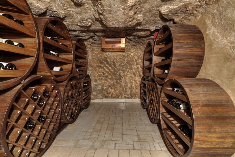 Underground wine cellar with round wooden racks and rustic stone walls.