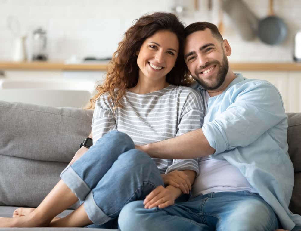 smiling couple sitting on sofa at home