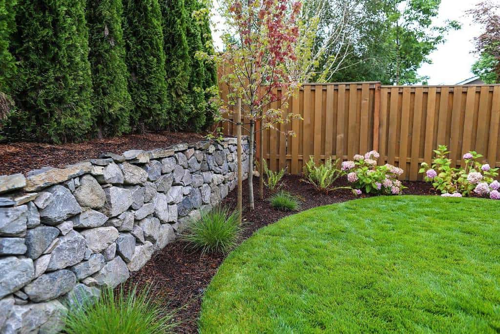 large backyard wood fence stone retaining wall grass area 