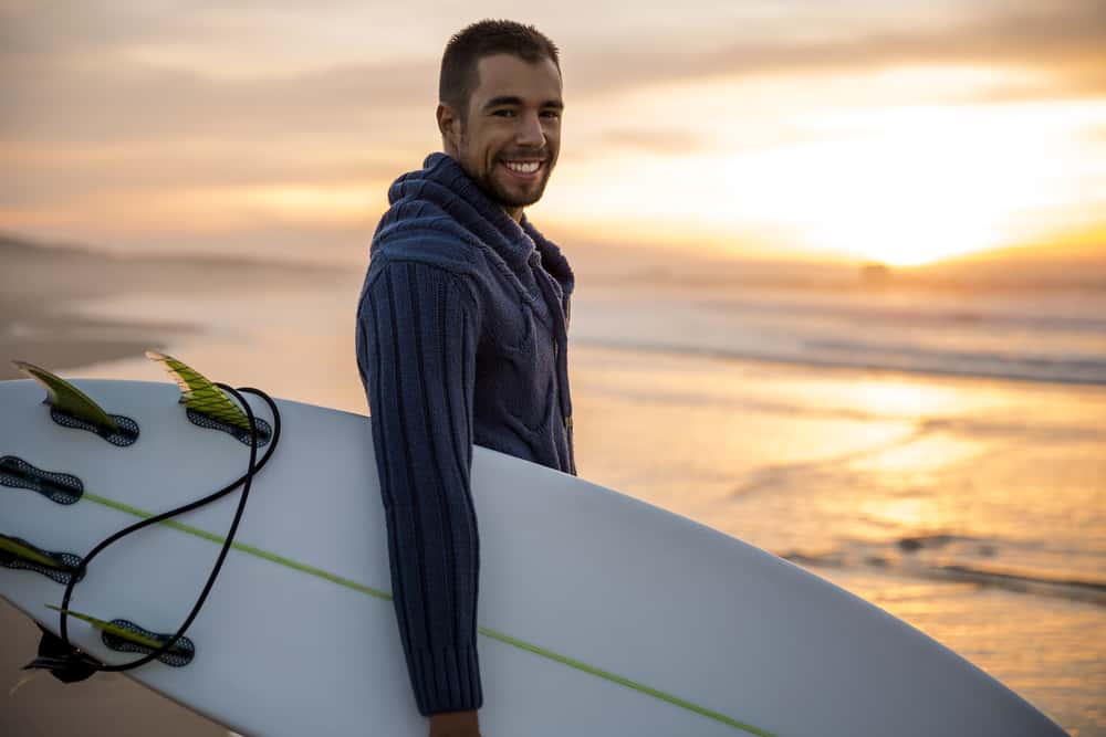 A surfer wearing a knit sweater holding his surfboard