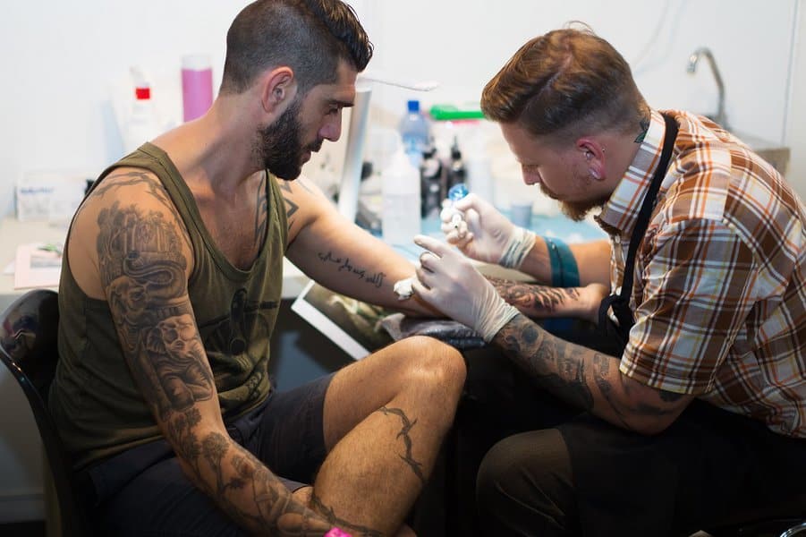tattoo artist doing tattoo on client arm