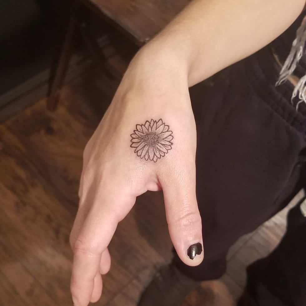 Hand tattoo between thumb and forefinger tiny black and grey daisy