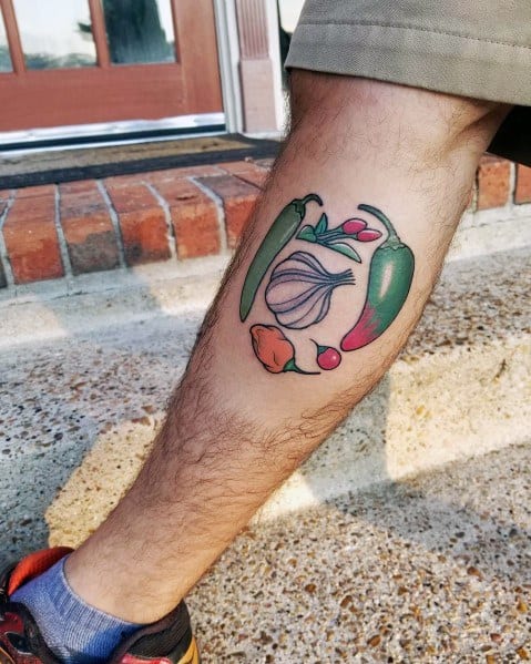 Colorful tattoo featuring chili peppers, garlic, and other spices in a circular arrangement, creating a vibrant and food-inspired design on the leg.