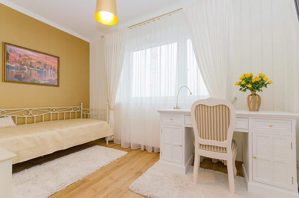 Bright bedroom with a mustard feature wall, white desk, airy curtains, and cozy rugs.