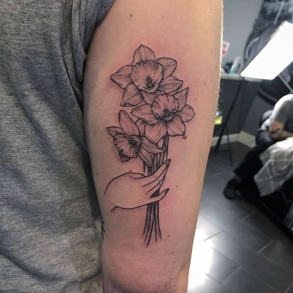 Trio Of Daffodils Cut Held By Dainty Hand Black And Gray Tattoo
