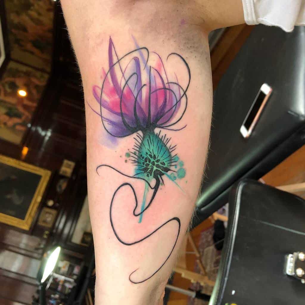 A delicate thistle-inspired tattoo with abstract flowers in vibrant pink, purple, and green hues graces a person's arm